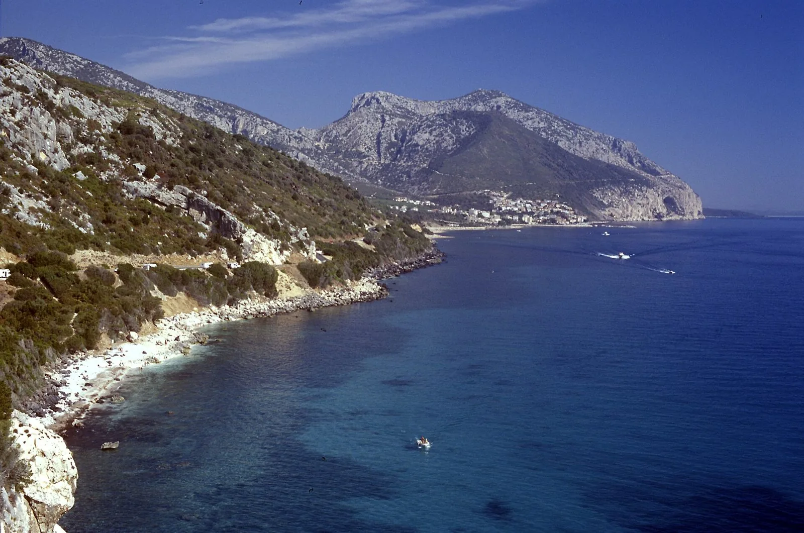 Costa rocciosa con acqua turchese e il paese di Cala Gonone ai piedi delle montagne calcaree